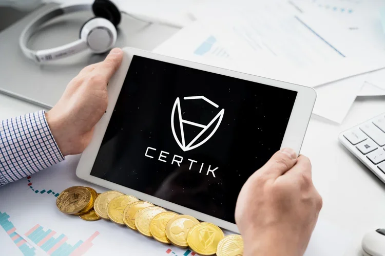 Логотип CertiK открыт на рабочем столе с монетками криптовалют.