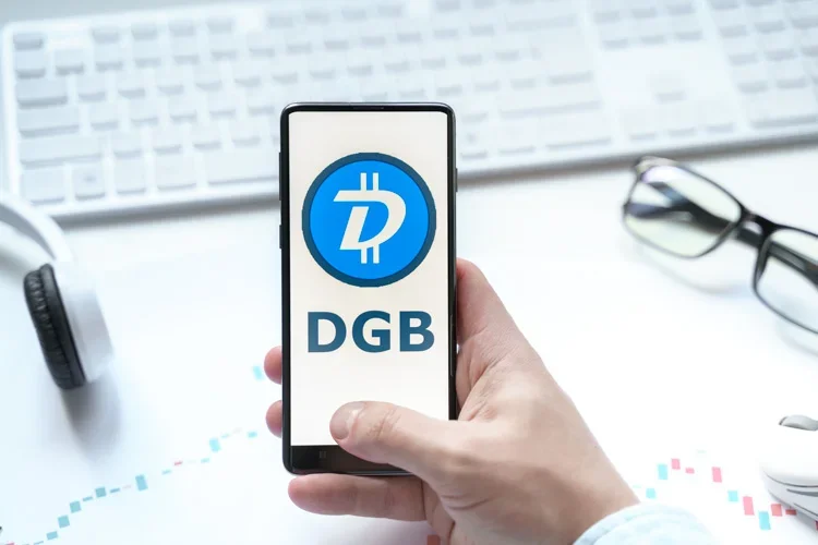 Монета DGB открыта на экране смартфона на фоне клавиатуры и наушников.