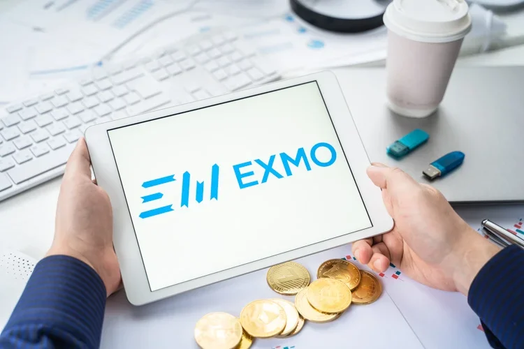 Криптобиржа EXMO открыта на экране планшета на фоне монет.
