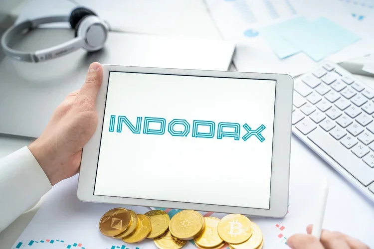 Криптовалютная биржа Indodax открыта на экране планшета с россыпью альткоинов внизу.