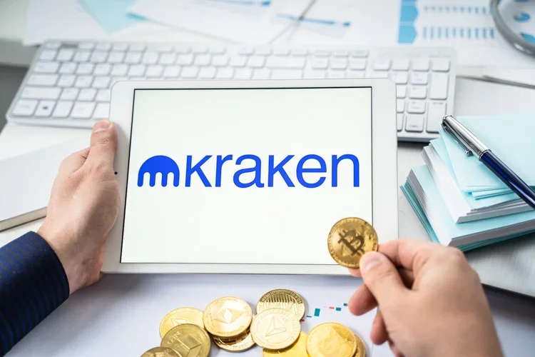 Монетка Bitcoin на фоне открытого на планшете Kraken.