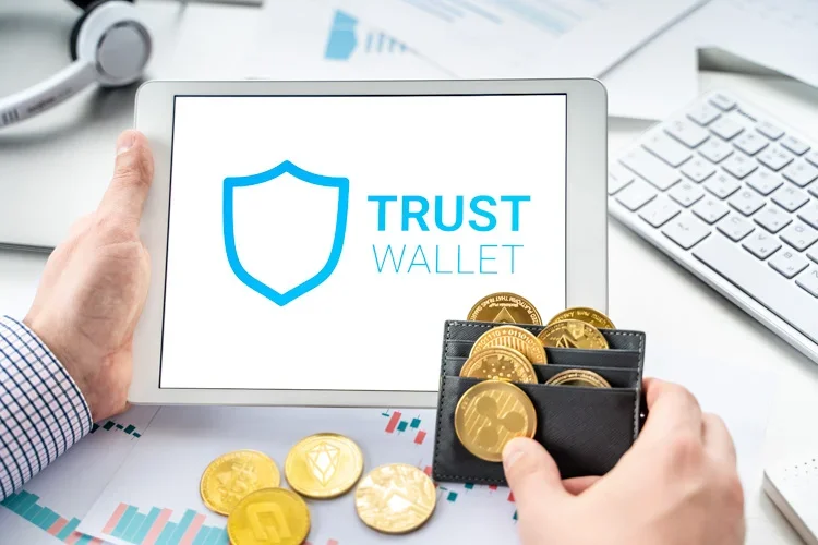 Trust Wallet открыт на экране планшета на фоне кошелечка, забитого монетками криптовалют.