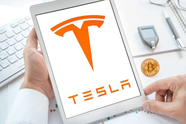 Логотип Tesla открыт на экране планшета с Bitcoin.