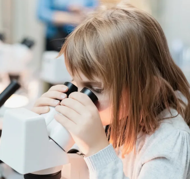 Девочка за микроскопом выполняет научный проект в школе.